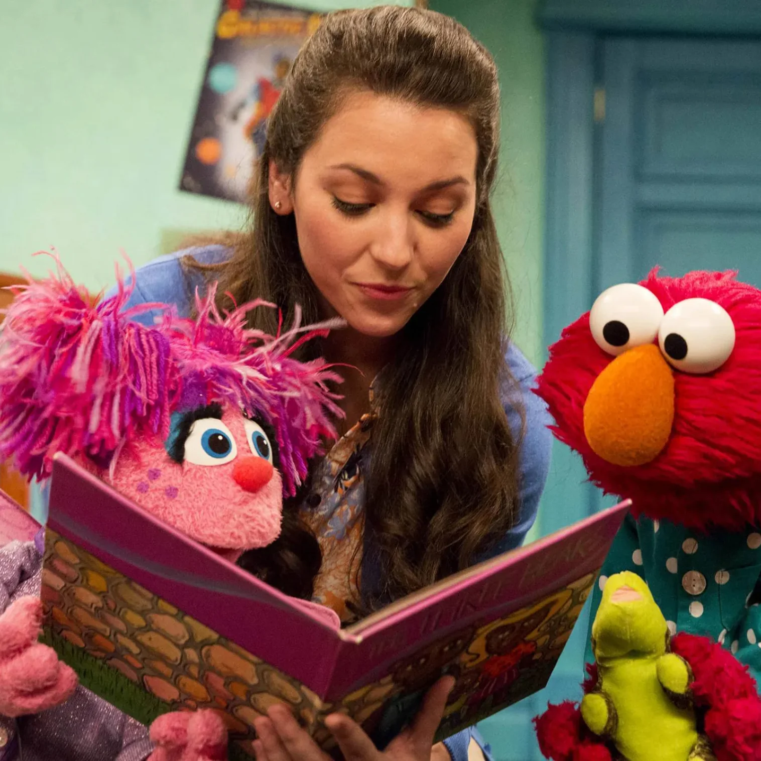 A woman reading a book with Elmo and Abby Cadabby
